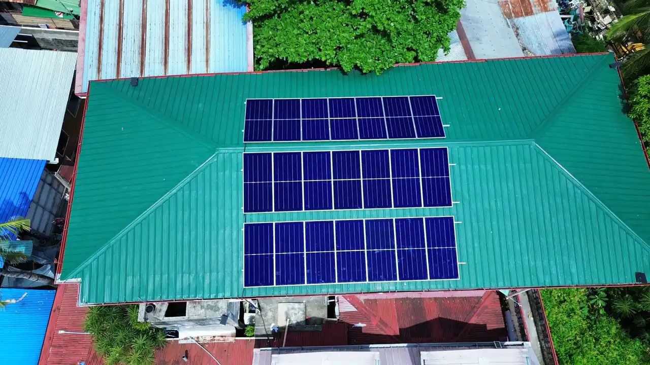 Aerial view of solar panels arranged across a large green metal roof